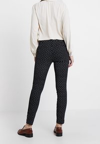 Leggings noirs à motifs avec des formes de diamants blanches, fabriqués en matériau extensible, associés à un haut de couleur claire et des chaussures marron.
