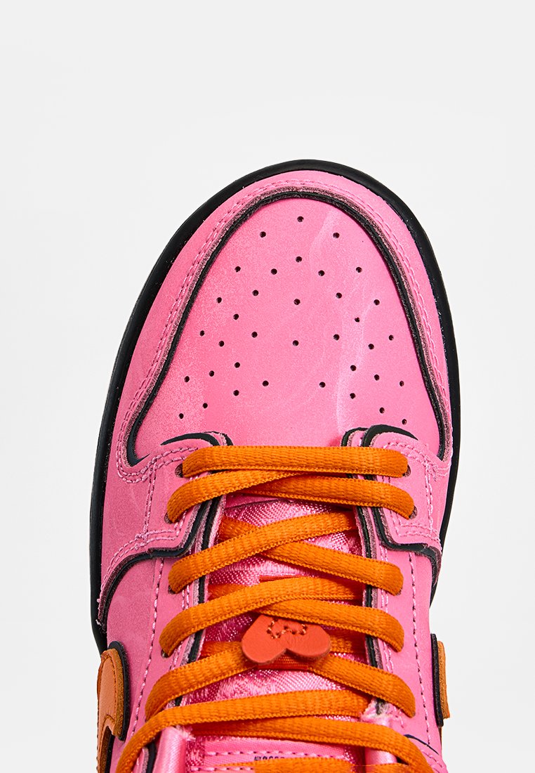 Baskets avec une tige en cuir rose brillant, bout perforé, lacets orange, semelle noire et accent en forme de cœur sur le lacet.
