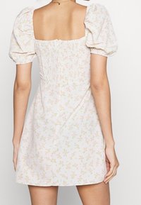 Robe à imprimé floral en rose clair avec un dos carré, des manches bouffantes et des détails froncés. Présente de petites fleurs et des accents verts.
