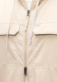 Μπεζ μπουφάν Columbia με δύο τσέπες με καπάκι, φερμουάρ μπροστά και λευκά κορδόνια με πλαστικές άκρες.