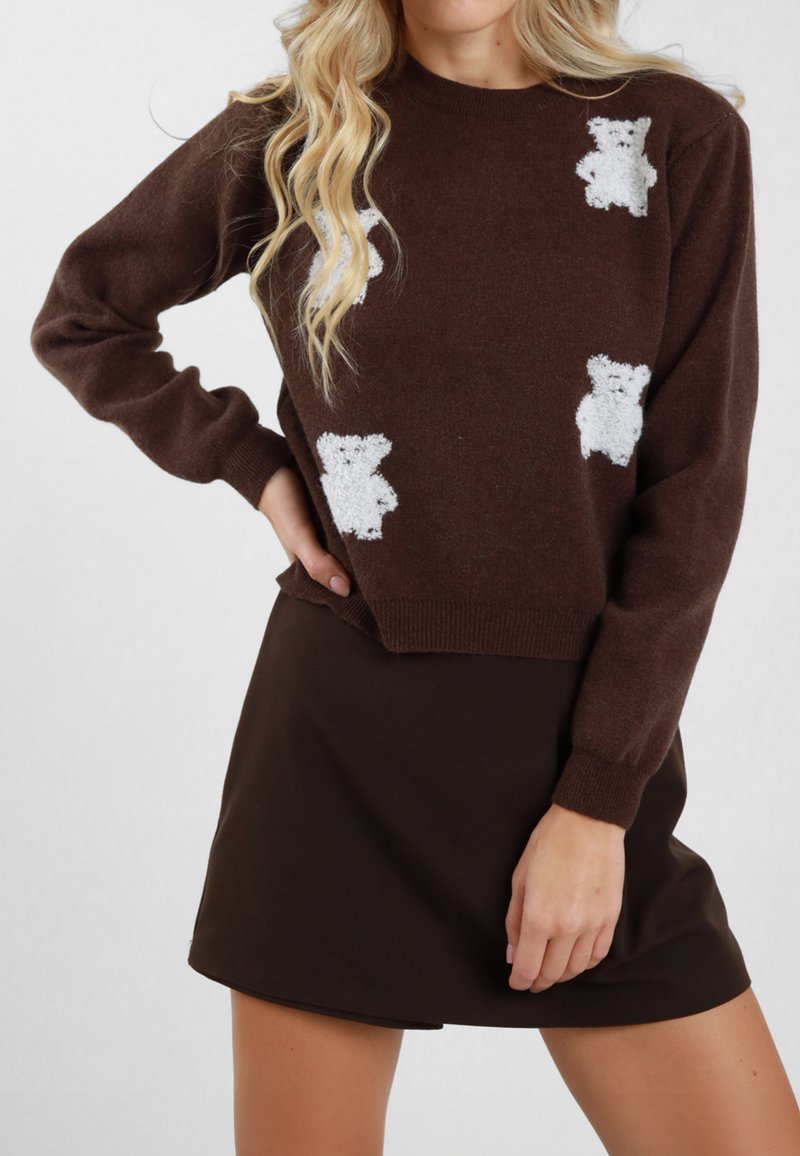 Maglione marrone lavorato a maglia con applicazioni di orsetti bianchi, collo rotondo e maniche lunghe, abbinato a una gonna scura. Tessuto morbido e strutturato.