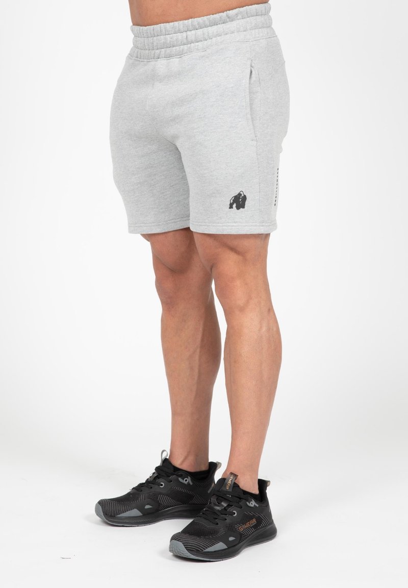 Grijze katoenmix shorts met een elastische band, zijzakken en een zwart gorilla-logo op het linkerbeen, gecombineerd met zwarte sportschoenen.