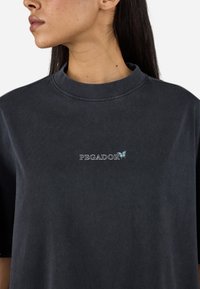 T-shirt surdimensionné gris foncé en coton, avec un col rond et un logo "PEGADOR" brodé avec un détail de papillon sur la poitrine.