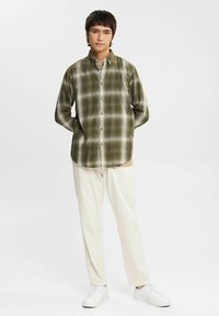 Green checkered button-up shirt, long sleeves, featuring a collar. Paired with cream-colored pants and white sneakers. Minimalist design.