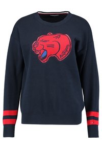 Pull bleu marine avec des poignets rayés rouges et un grand graphique de panthère rouge sur le devant. Le tissu est texturé avec une coupe décontractée.