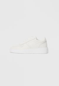 White sneakers with a smooth upper, perforated detailing, and a thick white sole. Features simple lacing and a rounded toe design.