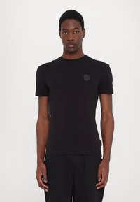 Tricou negru ajustat dintr-un material fin, cu decolteu rotund și mâneci scurte, ce prezintă un emblema texturată pe piept.