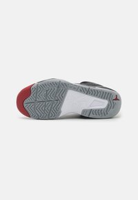 Suela de zapatilla negra con acentos en rojo y gris. Presenta un caucho texturizado, con surcos circulares y diagonales para tracción, y la marca "Nike Air".