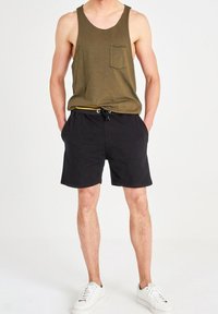 Débardeur vert olive avec poche, associé à un short noir à cordon de serrage. Des baskets blanches complètent le look. Design simple, coupe décontractée.