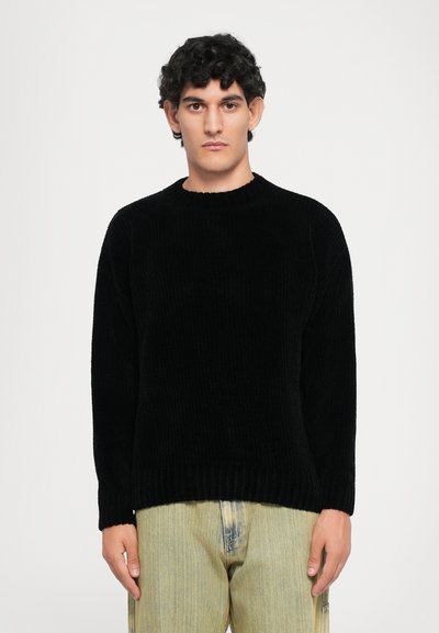 Black ribbed knit sweater with a round neckline, long sleeves, and a relaxed fit, paired with light denim pants.