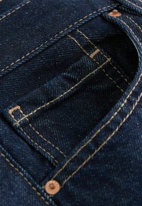 Tumedast sinise denim kangast, millel on nähtavad kontrastset värvi õmblused, väike tasku ja metallnupp.