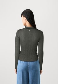 Dunkelgrünes geripptes Langarmoberteil mit enganliegender Silhouette, das einen kleinen Metallelement auf der Rückseite und einen subtilen Glanz im Stoff zeigt.