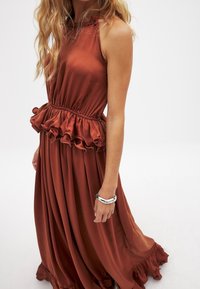 Robe couleur rouille avec un col halter, une taille froncée et une jupe fluide. Fabriquée en tissu lisse avec une texture douce et un ourlet ondulé.