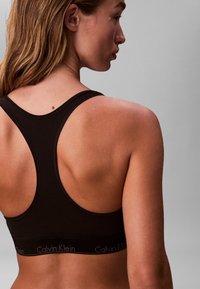 Schwarzer Sport-BH mit Racerback-Design und einem elastischen Band mit dem Schriftzug "Calvin Klein" in Grau. Glattes Material mit minimalen Nähdetails.