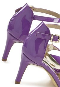 Sandali con tacco alto in pelle verniciata viola, con una sottile cinghia alla caviglia, hardware in argento e un ciondolo circolare attaccato.