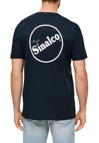 Tamsiai mėlynas medvilninis marškinėliai su apvaliu baltu logotipu ant nugaros, kuris skaito "Sinalco," su trumpomis rankovėmis ir apvaliu kaklu.
