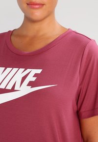 Bordová tričko vyrobené z hladké tkaniny s velkým bílým logem "NIKE" na přední straně a klasickým kulatým výstřihem.