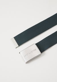 Zelený tkaný pásek s kovovou sponou stříbrné barvy, na které je vyraženo "JACK&JONES." Má ploché konce a texturovaný povrch.