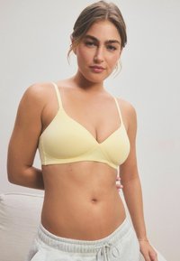 Sutien galben deschis, fără cusături, cu bretele ajustabile, într-o formă triangulară și cu o textură netedă, asortat cu pantaloni de trening gri.