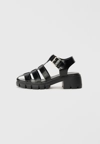 Sorte hælede sandaler med en blank finish, der har flere remme, en ankelspænde og en chunky gummisål med takket detaljer.