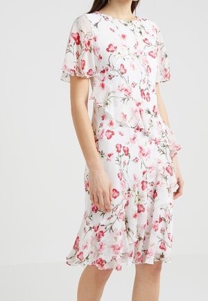 Robe blanche avec imprimé floral rose, manches évasées et détails de volants superposés asymétriques sur la jupe et le torse.