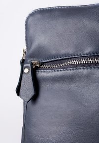Navy leather bag with a smooth texture, featuring a silver zipper and a tab for easy opening; close-up view of zipper and stitching details.