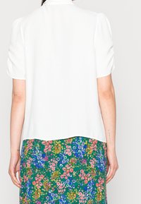 White short-sleeve blouse with a smooth texture and slightly puffed sleeves, paired with a floral-patterned green skirt.
