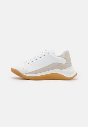 Witte sneaker met beige suède accenten en een zool van natuurrubber, voorzien van vetersluiting en een chunky, gebogen middenzool ontwerp.