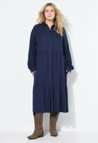 Marineblauwe kraagjurk met lange mouwen, gelaagd ontwerp en een relaxte pasvorm, gecombineerd met bruine cowboylaarzen. Geverfde stof met een gladde afwerking.
