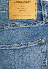 Ljusblå denimjeans har en läderpatch med varumärket "JACK & JONES" och sömnadsdetaljer, inklusive en enda bakficka.