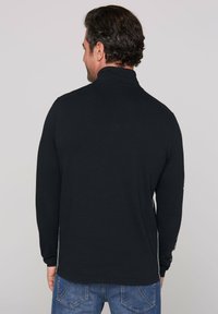 Camisa de manga larga en tejido negro sólido con un cuello alto, que presenta detalles contrastantes en los lados y un corte relajado.