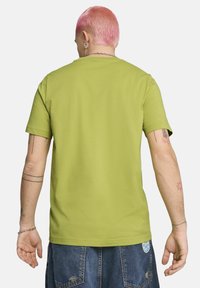 Camiseta verde de manga corta hecha de algodón, con cuello redondo. La vista trasera muestra una textura suave y un diseño simple sin estampados ni adornos.