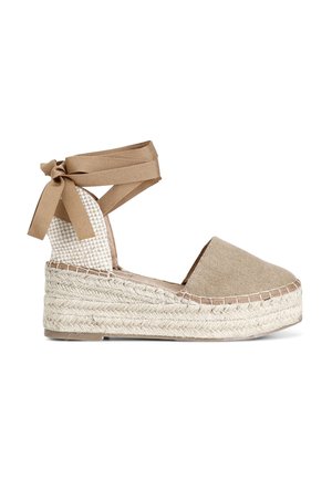 Bruine stoffe espadrille-wedge met een geweven juten zool. Voorzien van een enkelbandje met lintstrikjes en een gemustreerd textiel rugpaneel.
