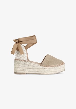 Bruine stoffe espadrille-wedge met een geweven juten zool. Voorzien van een enkelbandje met lintstrikjes en een gemustreerd textiel rugpaneel.