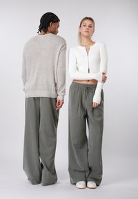 Világosszürke kötött pulóver kerek szegéllyel, olivazöld csíkos bő szárú nadrággal és fehér bebújós cipővel párosítva. Cipzár részlet a pulóveren.