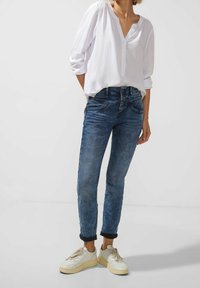 Blå denimjeans med slim fit, med hög midja, uppvikta benslut och subtila blekningar. Pairat med en lös vit knäppblus och sneakers.