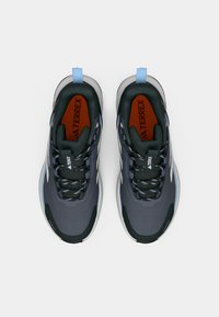 Γκρι αθλητικά παπούτσια με σκουροπράσινες λεπτομέρειες, στρογγυλή μύτη, υφασμάτινη επιφάνεια και ανθεκτική λαστιχένια σόλα. Διαθέτουν μπλε ταμπελάκι στη φτέρνα και κορδόνια με σχέδιο.