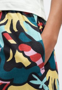 Πολύχρωμη φούστα με σχέδια που περιλαμβάνουν αφηρημένα σχήματα σε τιρκουάζ, κίτρινο, κόκκινο και μαύρο. Κατασκευασμένη από απαλό ύφασμα με χαλαρή εφαρμογή και πλαϊνές τσέπες.