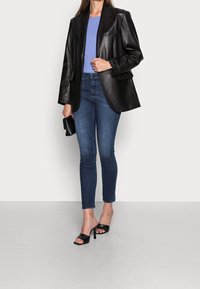 Blazer de cuero negro con solapas anchas, combinado con una camisa de color azul claro. Jeans de denim oscuro ajustados y sandalias de tacón negras.