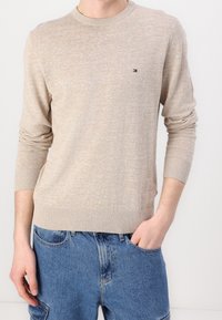 Beige neulepaita, jossa on pitkät hihat ja pyöreä kaula-aukko. Rinnassa on pieni logo, joka on punainen, valkoinen ja sininen. Teksturoitu kangas.