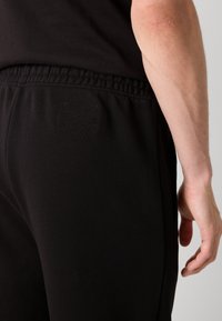 Zwarte sweatpants met een elastische tailleband, voorzien van een subtiele textuur logo patch op de achterkant en gladde stof voor comfort.