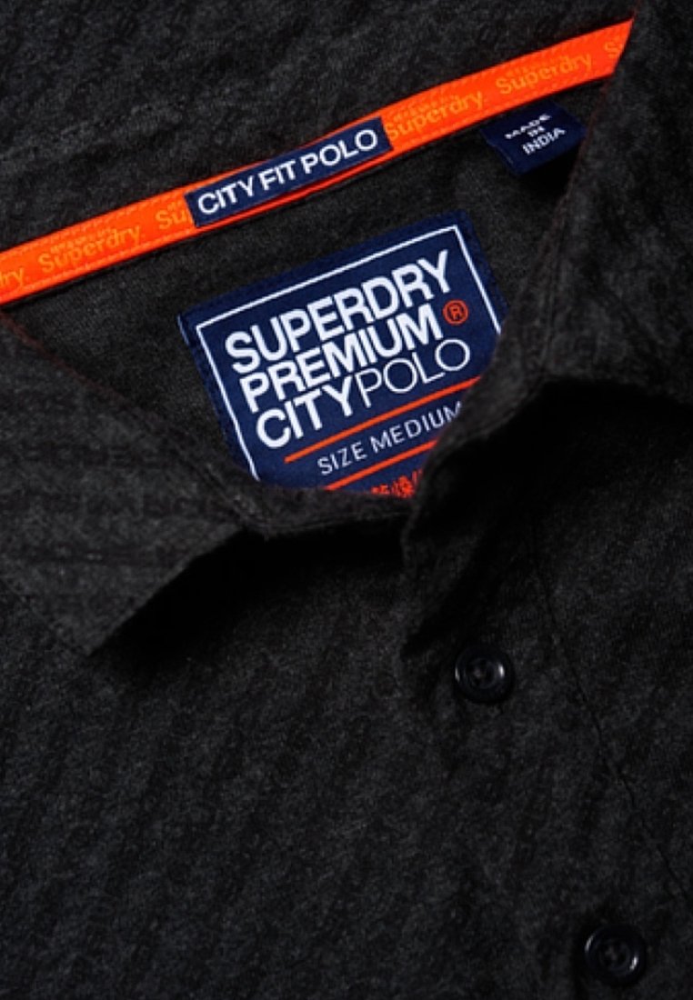Col de chemise texturé foncé avec étiquette Superdry Premium City Polo, taille moyenne, et une bande intérieure orange portant l'inscription Superdry.