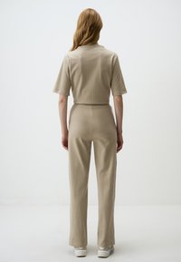 Beige ribbed two-piece set featuring a short-sleeve top and wide-leg pants, made from textured fabric. White sneakers complete the look.