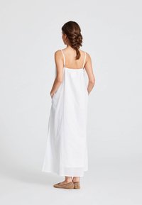 Rochie lungă albă, fără mâneci, cu bretele ajustabile și buzunare laterale. Fabricată dintr-un material ușor, având o croială lejeră și un design fluid.