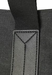 Nahaufnahme eines schwarzen Stoffriemens, der an einem strukturierten schwarzen Lederpatch auf einer dunklen Textiloberfläche genäht ist, wobei die detaillierte Nähte und Materialstruktur sichtbar sind.