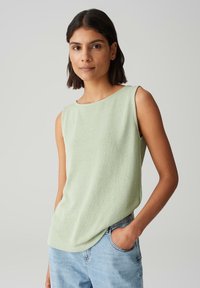 Top senza maniche verde chiaro realizzato in tessuto testurizzato, con scollatura rotonda e vestibilità morbida, abbinato a jeans azzurri chiari.