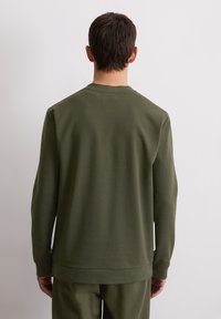 Sweatshirt vert foncé à col rond, manches longues et ourlet côtelé. Tissu lisse avec un minimum de détails, vu de dos.
