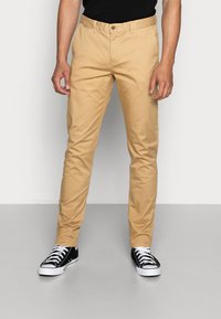 Beige chinos med slim fit, lavet af bomuldsblandingsstof. Har frontlommer, knaplukning og bæres med sort-hvide sneakers.