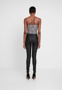 Grå spetskamisol med tunna axelband, parat med höga svarta leggings i faux läder och svarta högklackade skor.