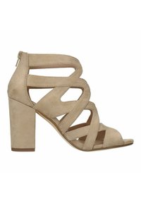 Beige suède blockhakken sandalen met open teen, voorzien van kruislingse banden en een zijrits voor eenvoudig aan- en uittrekken.